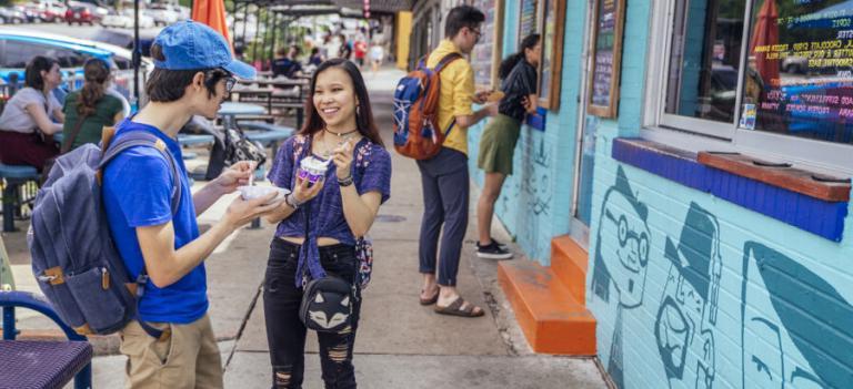 Two students order ice cream at a window in the background while two students enjoy their ice cream in the foreground on South Congress.