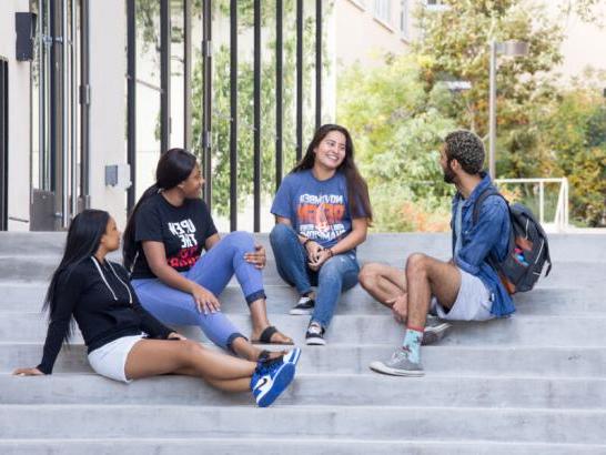 Four students sit on steps outside of St. Andre Apartments, hanging out and talking.